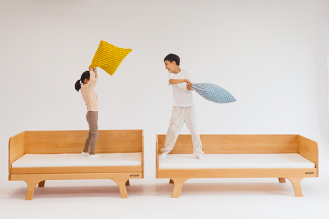 Avdar Home collection with two children having a pillow fight on separate natural wooden daybeds
