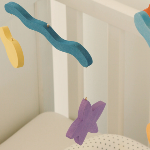 Close-up of blue wavy and purple star Wave Mobile pieces hanging beside a white crib