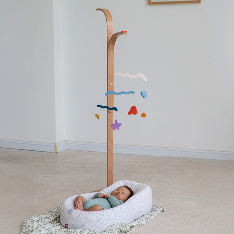 Tall wooden Wave Mobile stand with colorful hanging pieces above a baby in a bassinet
