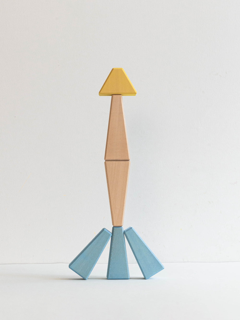 Wooden toy figure with a yellow head, brown torso, and blue legs on a light gray background