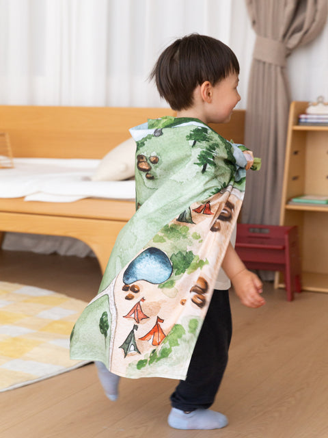 A child explores the Kingdom Valley play cloth as a cape, small-world play mat and imaginative backdrop with wooden toys.