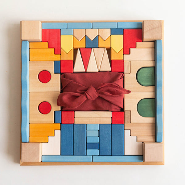 The Kingdom Block Set with colorful architectural wooden pieces and a red fabric bundle in a square tray