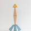 Wooden toy figure with a yellow head, brown torso, and blue legs on a light gray background