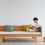 A child leaning on a beige Hug Hug Bed 90x200 , surrounded by pillows of different colors.
