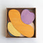 A collection of abstract shaped wooden blocks in various colors collected in a rectangular corrugated cardboard box.
