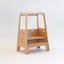 A beige wooden toddler tower with two platforms, designed for dual stability and adjustable heights.