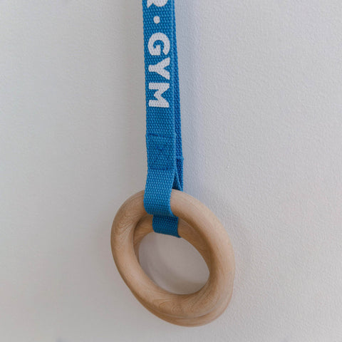 A wooden ring attached to a blue rope with the text 'AVDAR GYM' written on it, hanging against a white background.
