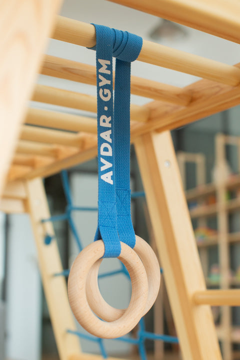 Wooden gymnastic rings with a blue strap hanging on the wooden climber