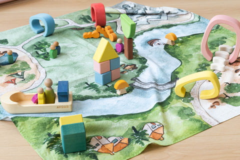 Close-up of wooden figures, boat, bridges and houses arranged on the Kingdom Valley play cloth