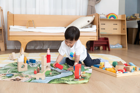 Child building a wooden block kingdom on the Kingdom Valley play cloth