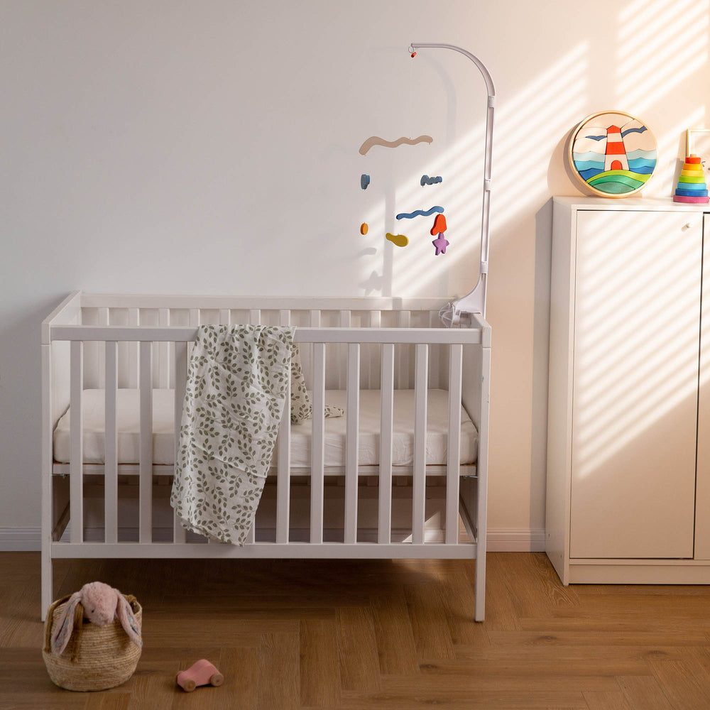 A colorful mobile toys are hanging above the bed, and two rainbow stacks are on the white table