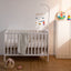 A colorful mobile toys are hanging above the bed, and two rainbow stacks are on the white table