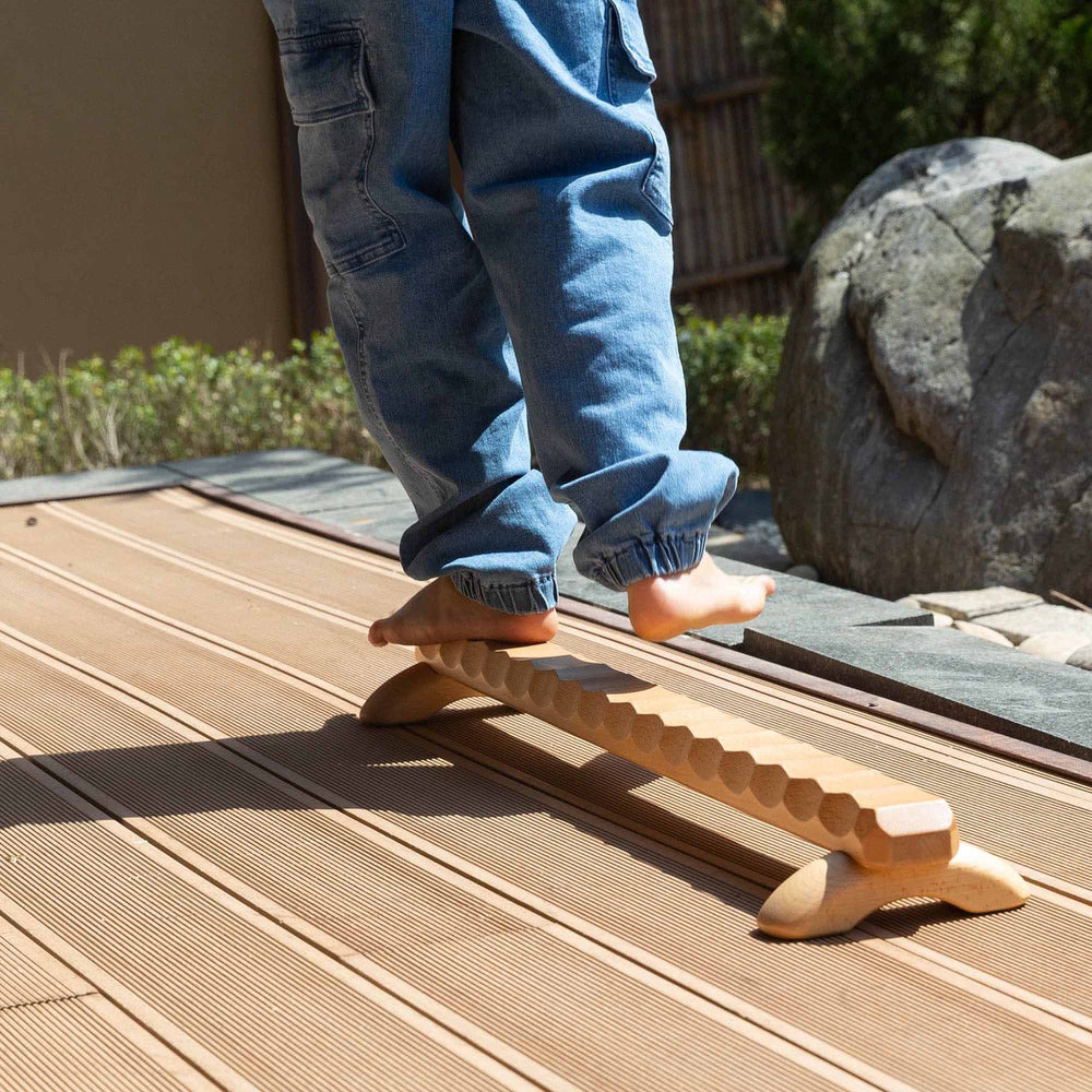 Child's feet on a wooden Naguri Balance Beam with a wavy surface designed for stimulation and massage.