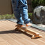 Child's feet on a wooden Naguri Balance Beam with a wavy surface designed for stimulation and massage.
