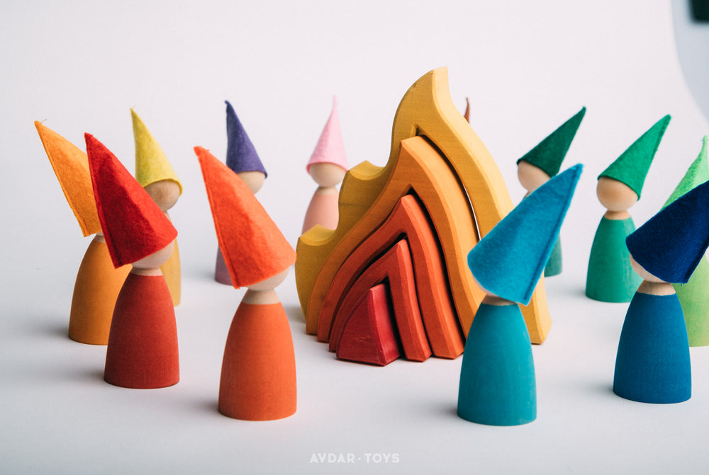 A set of colorful wooden peg dolls with different colored hats, standing around a wooden fire