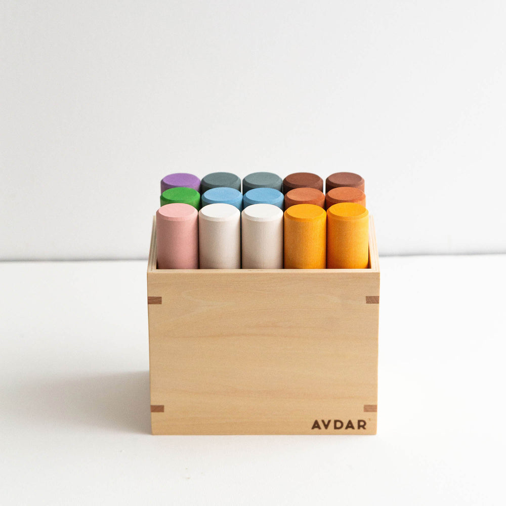 A set of colorful wooden cylinder blocks in various sizes, displayed both inside and outside of a wooden box. The cylinders are in multiple shades including green, yellow, blue, pink, orange, and gray.
