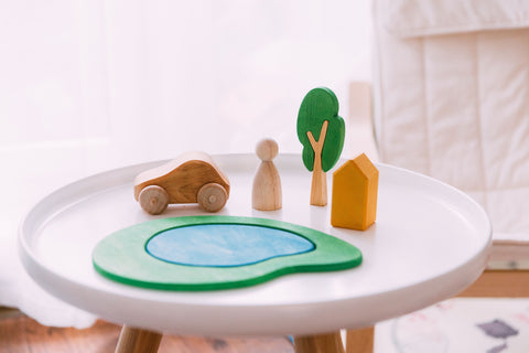 Wooden car,human, tree and house are on a small white coffee table 
