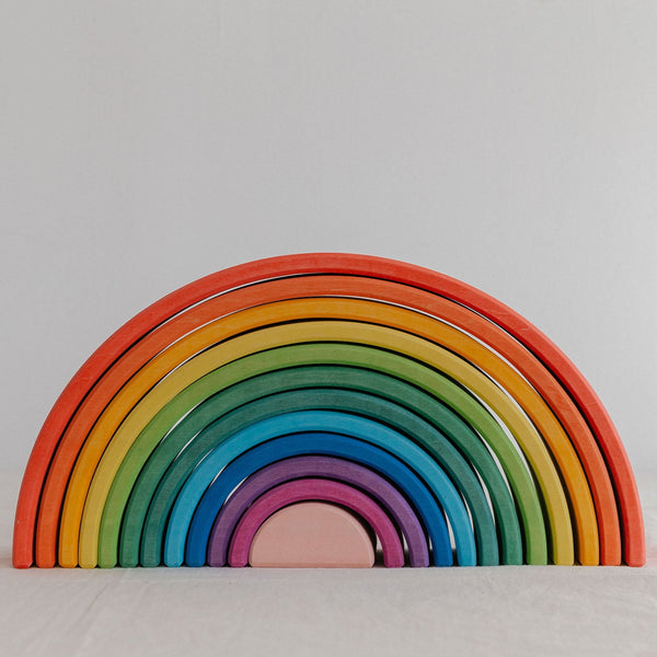 A colorful wooden rainbow stacker toy with multiple arches in various sizes arranged in a spiral pattern on a white background.